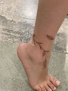 a woman's foot with a small tattoo on the side of her leg and leaves attached to it