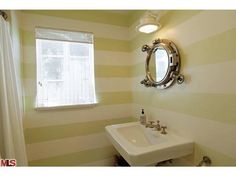 a white sink sitting under a mirror in a bathroom next to a window with striped walls