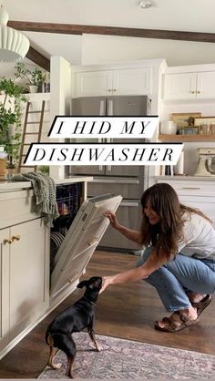 a woman is opening the dishwasher in her kitchen with a dog looking at it