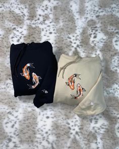 two sweatshirts with koi fish on them are laying on a white and gray surface