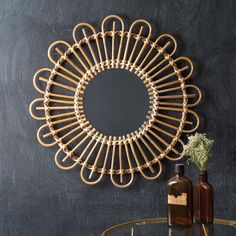 a round mirror hanging on the wall above a glass table with bottles and vases