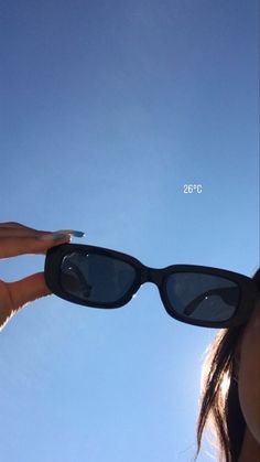 a woman wearing sunglasses looking up into the sky with her hand on top of her glasses