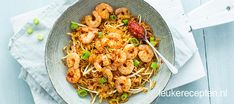 a bowl filled with shrimp and noodles on top of a white cloth next to a fork