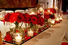 a long table with candles and red roses in glass vases on the tables are set up for a formal function