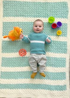 a baby laying on top of a blue and white blanket next to a yellow fish