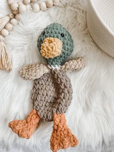 a crocheted stuffed duck laying on top of a white fur covered floor next to beads