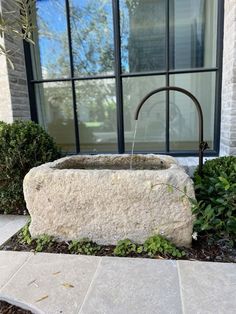 a stone fountain in front of a building with plants growing around it and an open window