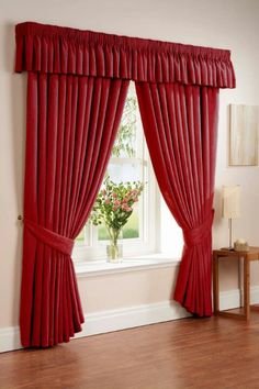 a red curtain with pleated drapes hanging in front of a window next to a wooden table