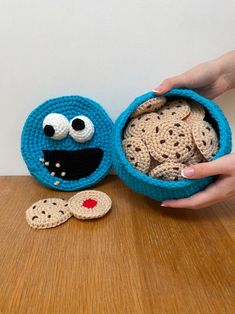 a crocheted cookie in a blue bowl next to a handmade cookie with eyes