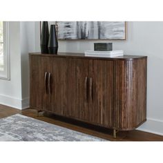 a wooden cabinet sitting in front of a window next to a rug and painting on the wall