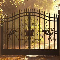 an iron gate in front of a tree with leaves on it and the sun shining through