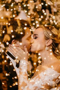 a bride and groom kissing in front of a christmas tree with lights all around them