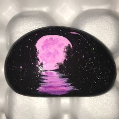 a painted rock sitting on top of white rocks with water and trees in the background