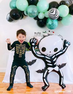 a young boy standing in front of a balloon arch with a skeleton costume on it