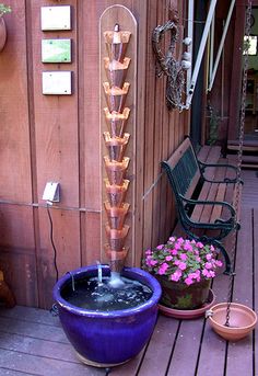 a water fountain sitting on top of a wooden deck next to potted plants and flowers