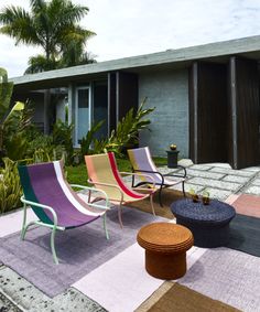 colorful lawn chairs and tables in front of a house with palm trees on the side