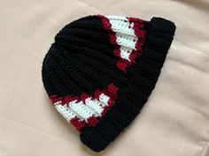 a crocheted black and white hat laying on top of a bed next to a pillow