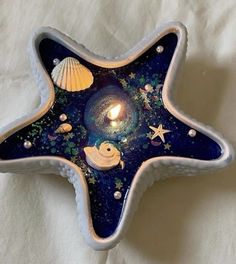 a starfish shaped candle holder with seashells and stars in the center on a white sheet