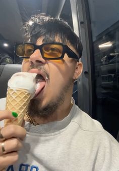 a man in sunglasses is eating an ice cream cone with his mouth open and tongue out