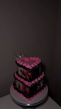 a three tiered cake with pink and black icing on the bottom, topped with a tiara