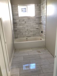 an empty bathroom with white marble tile flooring and bathtub in the corner between two doors