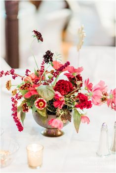 a vase filled with red and pink flowers on top of a white cloth covered table