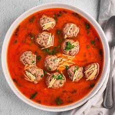 a bowl of soup with meatballs and pasta in it on a white table cloth