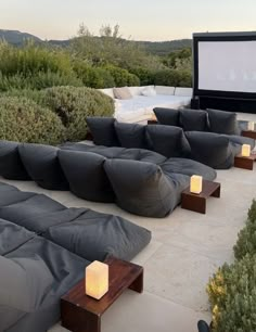 an outdoor seating area with couches and candles on the ground in front of a movie screen