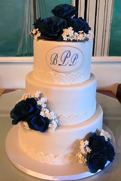 a three tiered wedding cake with blue flowers on the side and monogramming