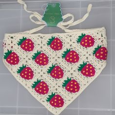 a crocheted bib with strawberries on it hanging from a hook in the bathroom