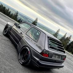 a car parked on the side of a road next to some trees and mountains in the background