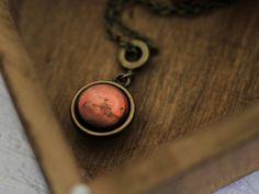 a necklace with an orange stone in it sitting on a wooden box next to a chain