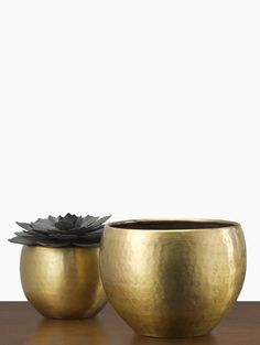 two gold bowls sitting on top of a wooden table next to each other and one has a black flower in it