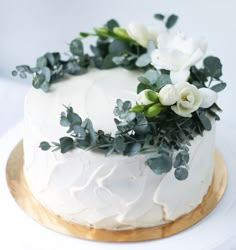 a white cake decorated with flowers and greenery on a gold plated platter