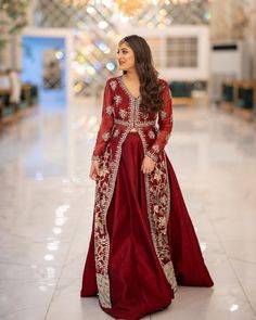 a woman in a red and gold gown standing on the floor with chandelier behind her