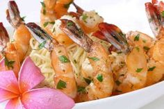 a bowl filled with shrimp and pasta next to a pink flower on a white surface