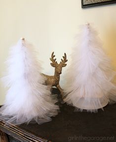 two white christmas trees with gold glitter antlers and tulle skirted tree toppers