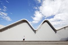 a person standing in front of a white building with two large triangular shaped windows on the side