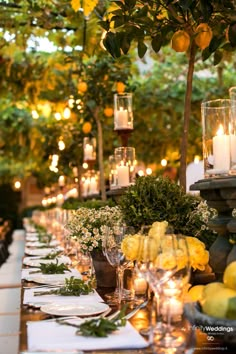 a long table with candles and lemons on it is set for an outdoor dinner