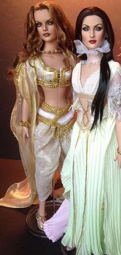 two dolls dressed in white and gold are standing next to each other on a table