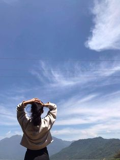 a woman standing on the side of a road holding her hat up to her head