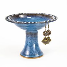 a small blue vase with a gold key hanging from it's side on a white background