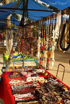 a red table topped with lots of bracelets and necklaces under a blue tent