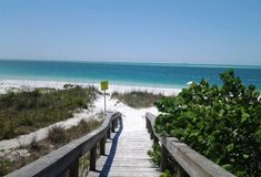 a wooden walkway leading to the beach with blue water and white sand in the background