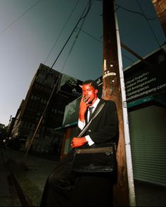 a man in a suit and tie sitting on a telephone pole talking on his cell phone