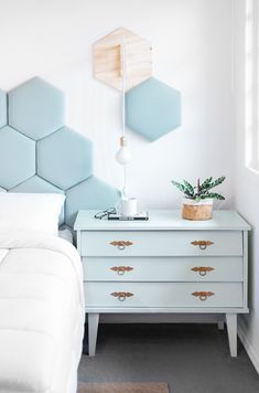 a white bed sitting next to a blue dresser with a plant on top of it