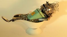 a white vase filled with assorted metal items on top of a table next to a wall