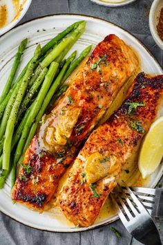 two salmons and asparagus on a white plate with lemon wedges next to them