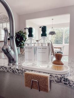 two bottles of hand soap sitting on top of a kitchen counter next to a brush