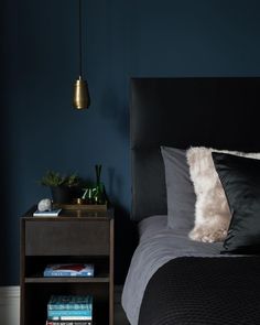 a bedroom with blue walls, black bedding and a gold lamp hanging from the ceiling